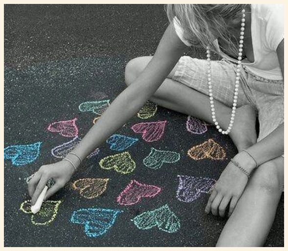 Una chica dibujando corazones con tiza en el suelo.