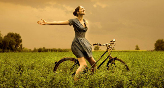Una donna felice, sul campo, con la sua bicicletta.